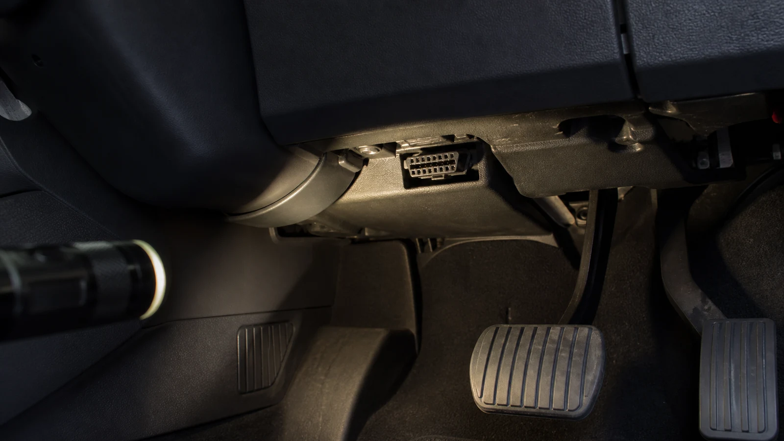 Driver-side footwell on a UK right-hand-drive car showing a typical OBD2 diagnostic port location
